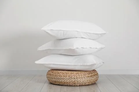 Stack of clean pillows on wicker pouf near white wall Stock Photos