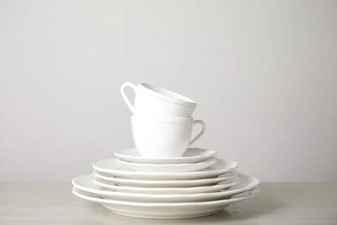 Stack of clean plates and cups on table against white background Stock Photos