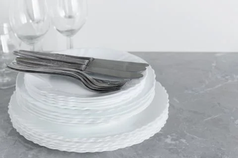 Stack of clean plates with forks, knives and glasses for serving on stone tab Stock Photos