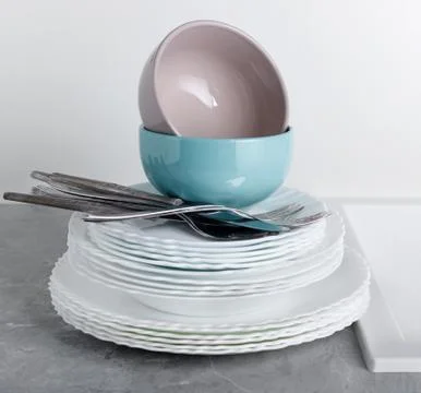 Stack of clean plates with forks, knives and glasses for serving on stone tab Stock Photos