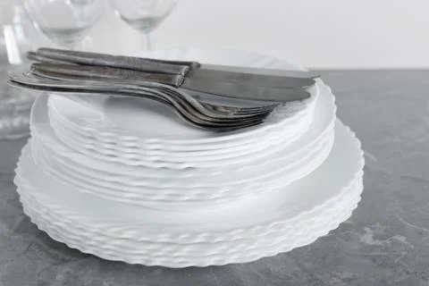 Stack of clean plates with forks, knives and glasses for serving on stone tab Stock Photos