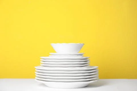 Stack of clean plates on white table against yellow background 스톡 사진