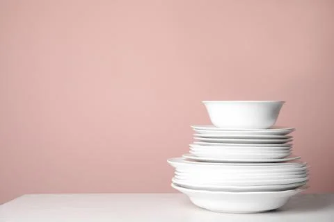 Stack of clean plates on white table against pink background. Space for text Stock Photos