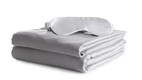 Stack of clean silky bed linen and sleeping mask isolated on white Stock Photos