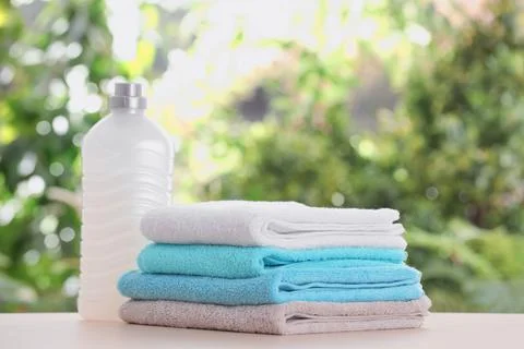 Stack of clean soft towels and laundry detergent on table against blurred bac Stock Photos