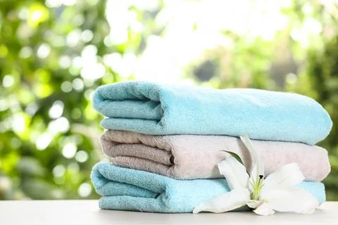Stack of clean soft towels and flower on table against blurred background Foto stock