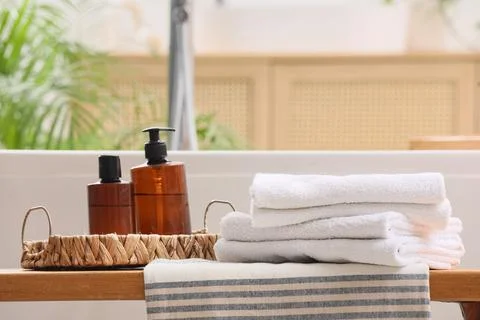 Stack of clean soft towels and bath supplies on bench in bathroom, closeup Stock Photos