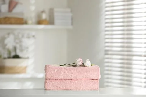 Stack of clean soft towels with eustoma flowers on white table indoors 스톡 사진