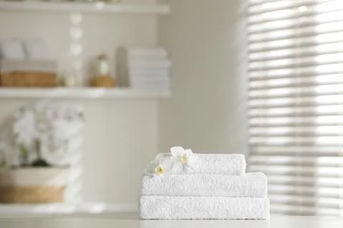 Stack of clean soft towels with orchid flowers on white table indoors 스톡 사진