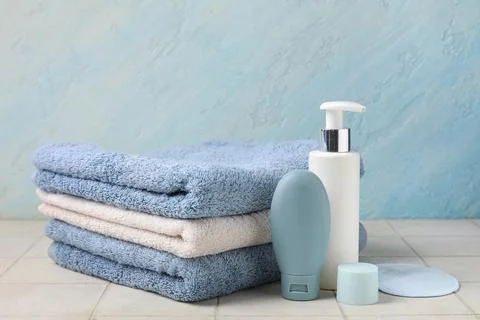 Stack of clean towels and cosmetic products on light tile table against color Stock Photos