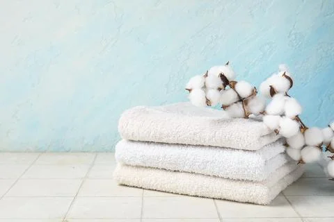 Stack of clean towels and cotton branch on light tile table against color wal Stock Photos