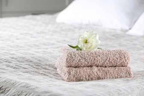 Stack of clean towels and Eustoma flower on bed, space for text 스톡 사진