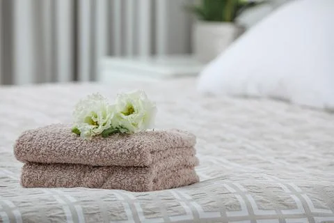 Stack of clean towels and Eustoma flowers on bed indoors, space for text Foto stock