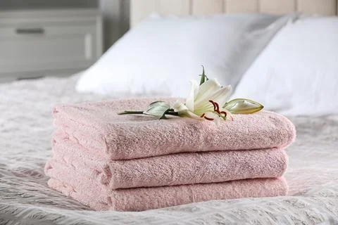 Stack of clean towels and flower on bed indoors 스톡 사진