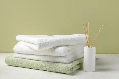 Stack of clean towels and reed diffuser on light table near color wall Stock Photos