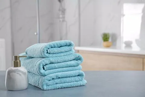 Stack of clean towels and soap dispenser on grey stone table in bathroom. Spa 스톡 사진