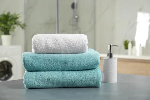 Stack of clean towels and soap dispenser on grey stone table in bathroom 스톡 사진