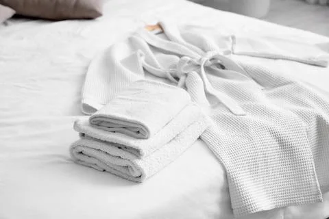 Stack of clean towels with bathrobe on bed in hotel room Stock Photos