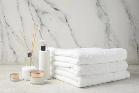 Stack of clean towels, cosmetic products and reed diffuser on light backgroun Stock Photos