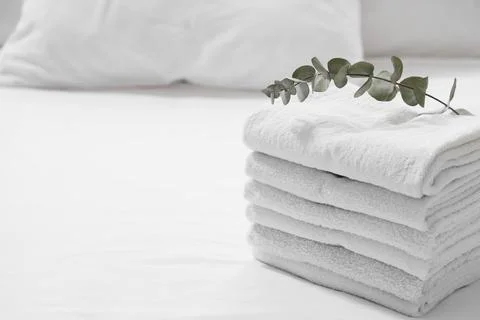 Stack of clean towels with eucalyptus branch on bed in hotel room Stock Photos