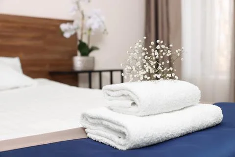 Stack of clean towels with flowers on bed in hotel room 库存照片