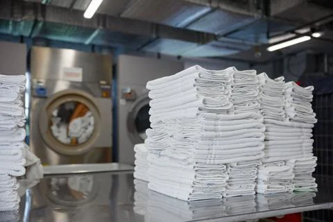 A stack of clean towels is on a table in front of a washing machine Stock Photos