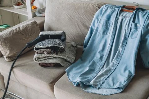 A stack of clean warm clothes and shirt with a steam cleaner on Stock-Fotos