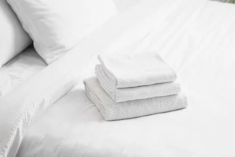 Stack of clean white folded towels on a freshly made with white sheets and pi Stock Photos