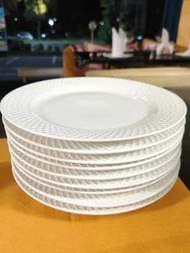 A stack of clean white plates with a patterned rim on an orange tablecloth Stock Photos