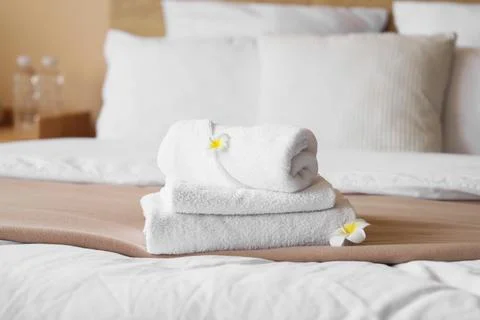 Stack of clean white towels with frangipani flowers on a hotel bed, hospitali Stock Photos