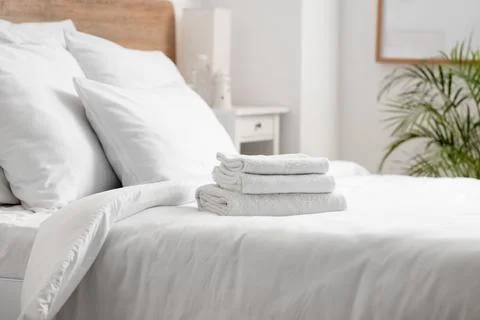 Stack of clean white towels on a freshly made bed with white linens and pillo Stock Photos