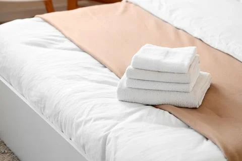 Stack of clean white towels on a hotel bed with fresh linens, Hospitality and Stock Photos