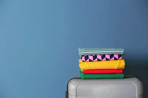 Stack of clothes on suitcase against color background Stock Photos
