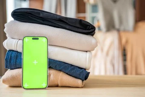 Stack of clothing prepared for resale with a smartphone displaying green screen Stockfoto's