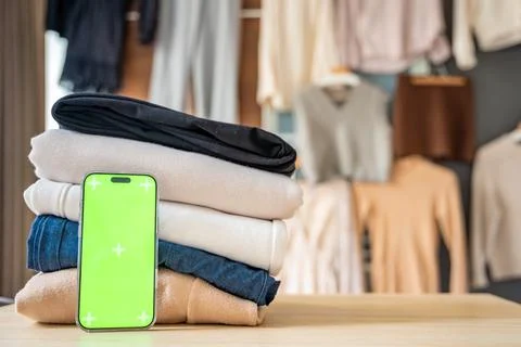 Stack of clothing prepared for resale with a smartphone displaying green screen Stockfoto's