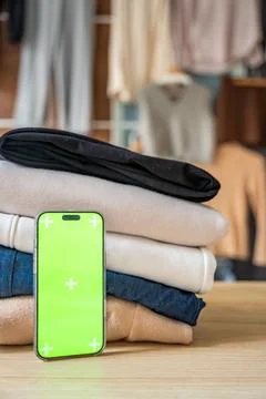 Stack of clothing prepared for resale with a smartphone displaying green screen Stockfoto's