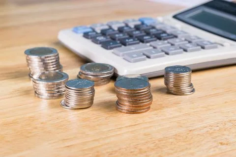 Stack of coin with blurred calculator for blackground on wood table Photos