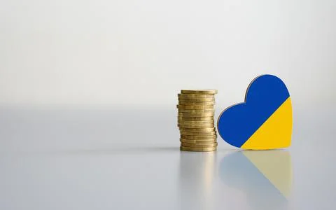 A stack of coins and the flag of Ukraine in the shape of a heart. Stock Photos