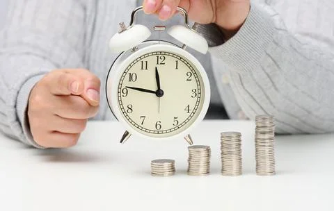 Stack of coins and round white alarm clock on the table. The concept of time  Stockfoto's