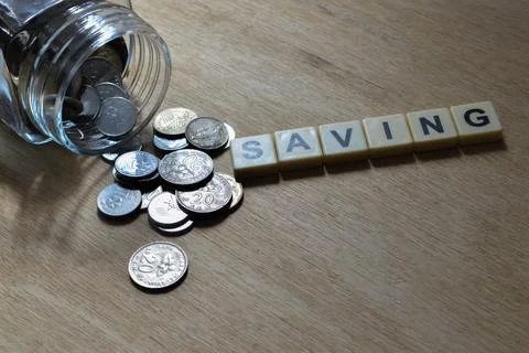 Stack of coins and scrabble letters with text SAVING over wooden background. Stock Photos