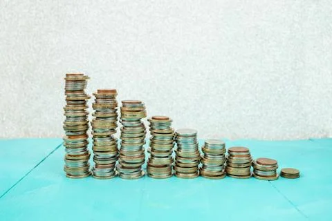 Stack of coins bar chart graph trending downwards with white wall backgroun.. 库存照片