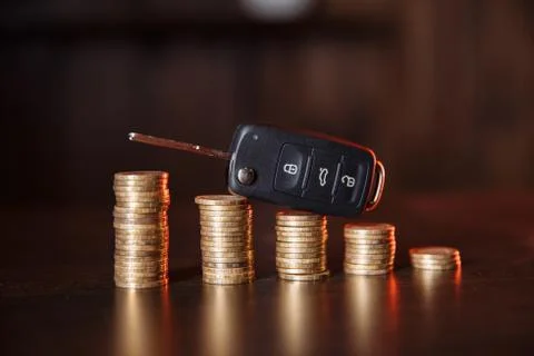 Stack of coins with black car key placed on desk Stock Photos
