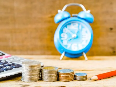 Stack of coins with calculator, red pencil and alarm clock on wooden backgrou Stock Photos