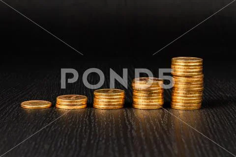 Stack of coins lie on a black wooden table Stock Photos