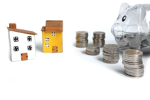 Stack of coins next to a clear piggy bank and miniature houses Stock Photos
