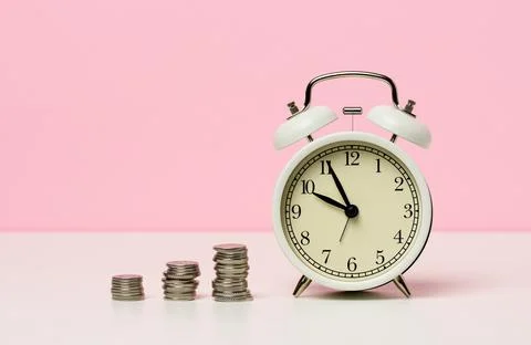 Stack of coins round white alarm clock on the table. The concept of time is m Stock-Fotos