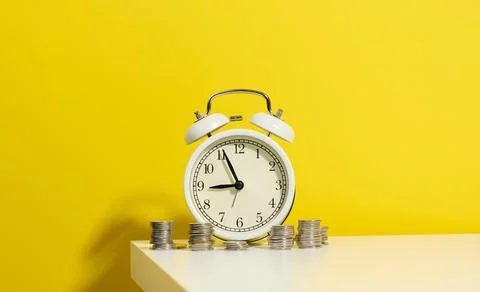 Stack of coins round white alarm clock on the white table. The concept of tim Stockfoto's