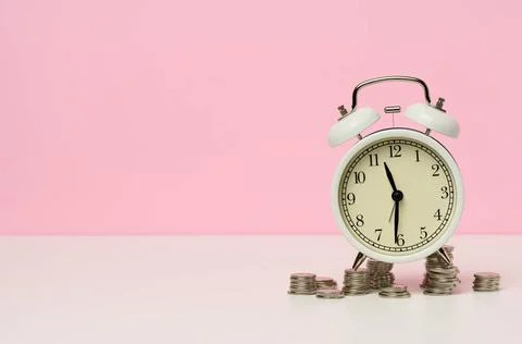 Stack of coins round white alarm clock on the table. The concept of time i... Stock Photos