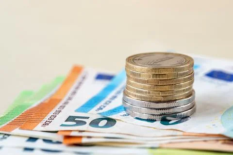 Stack of coins on several euro banknotes on a beige tabletop. Stock Photos
