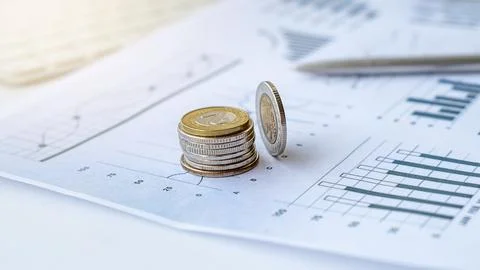 A stack of coins sits on a financial chart with a pen resting on the side. Th Stock Photos
